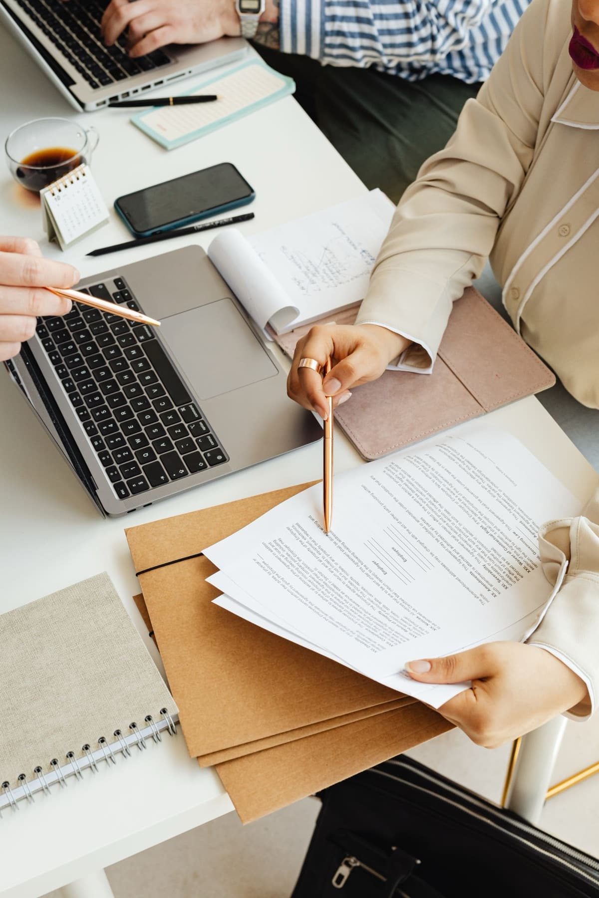Autour d'une table, deux personnes annotent au crayon des documents posés sur des chemises en carton.