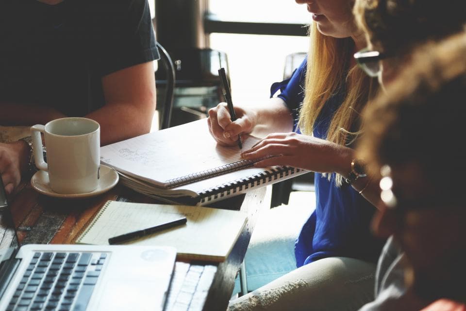 Trois personnes réunies autour d'une table de travail, carnets et ordinateur