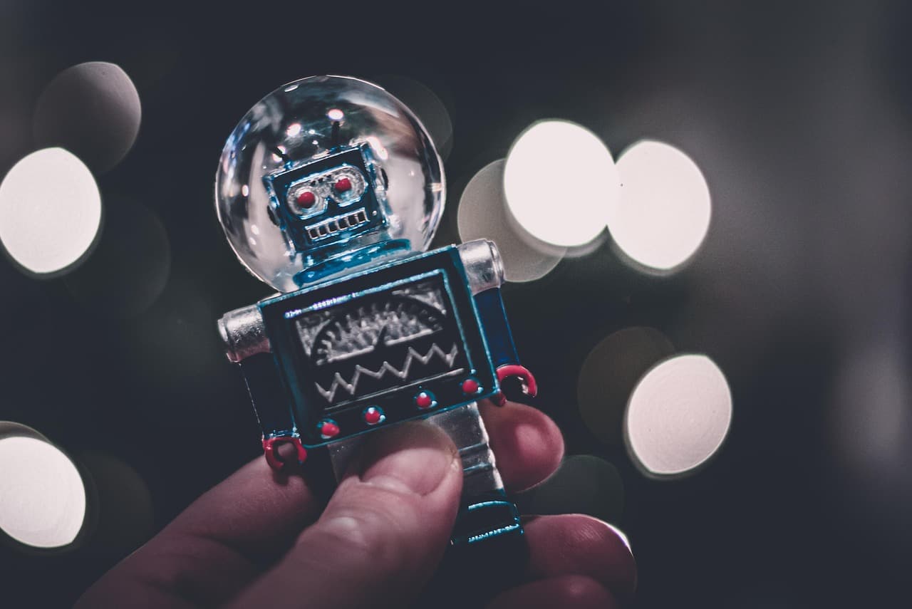 Une main tient un petit robot jouet en métal, devant des lumières floues