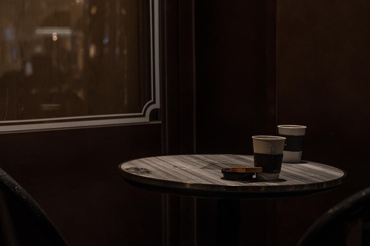 Deux gobelets de café posés sur une petite table ronde en bois, dans un café à la lumière tamisée