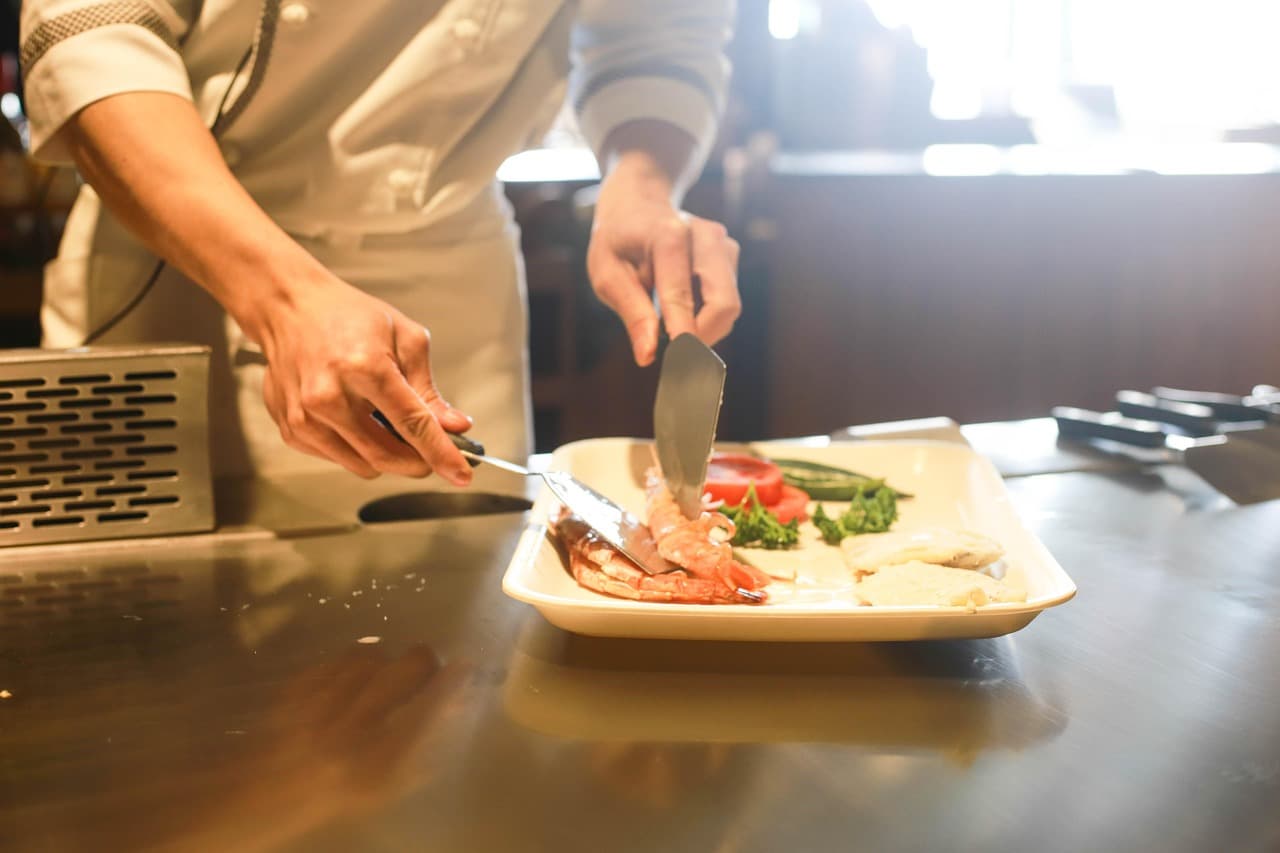 Cuisinier en veste blanche qui dresse une assiette sur un plan de travail en inox