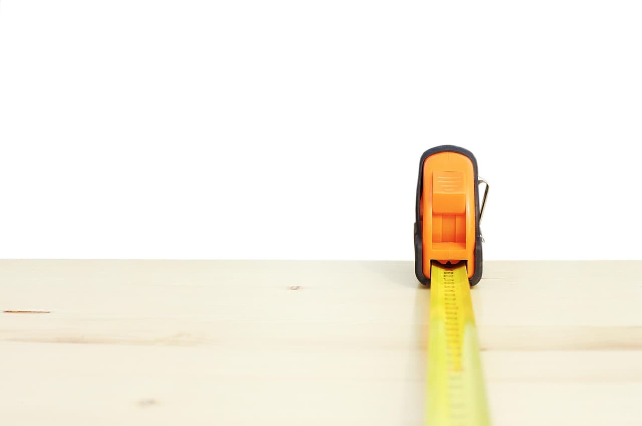 Un mètre ruban orange déroulé sur une planche de bois clair