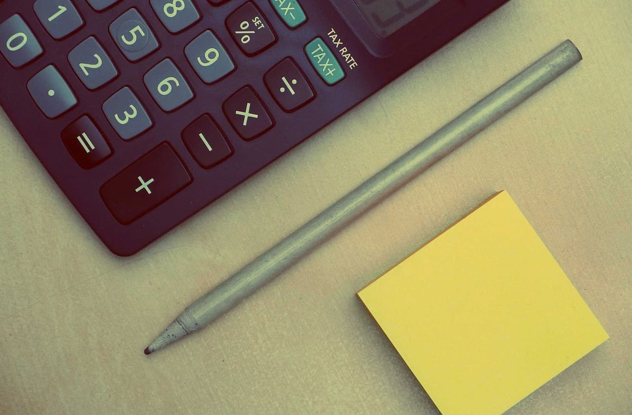 Une calculatrice, un crayon et un bloc-notes jaune posés sur un bureau