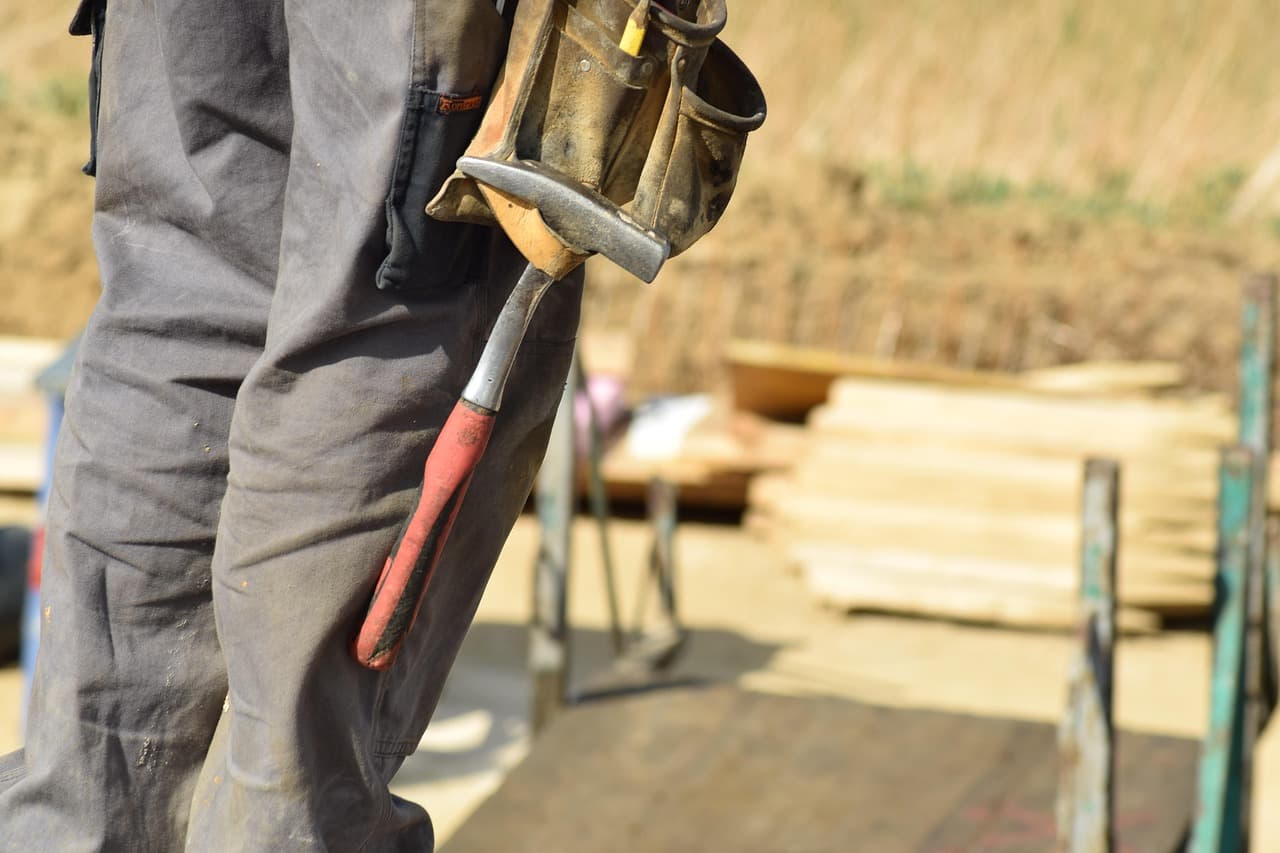 Ouvrier de chantier de dos, marteau à la ceinture, devant des matériaux de construction